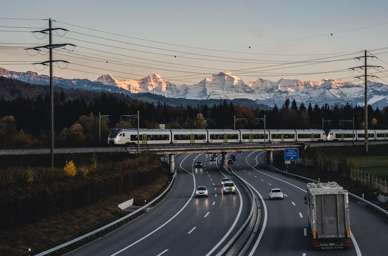 Autoroute et train régional côte à côte devant les Alpes, illustration de la mobilité multimodale