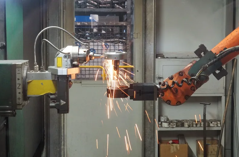 Robot industriel orange en cours d’usinage, gerbe d’étincelles