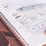 Croquis de maquette d'application sur un carnet à spirale, à côté d'un smartphone