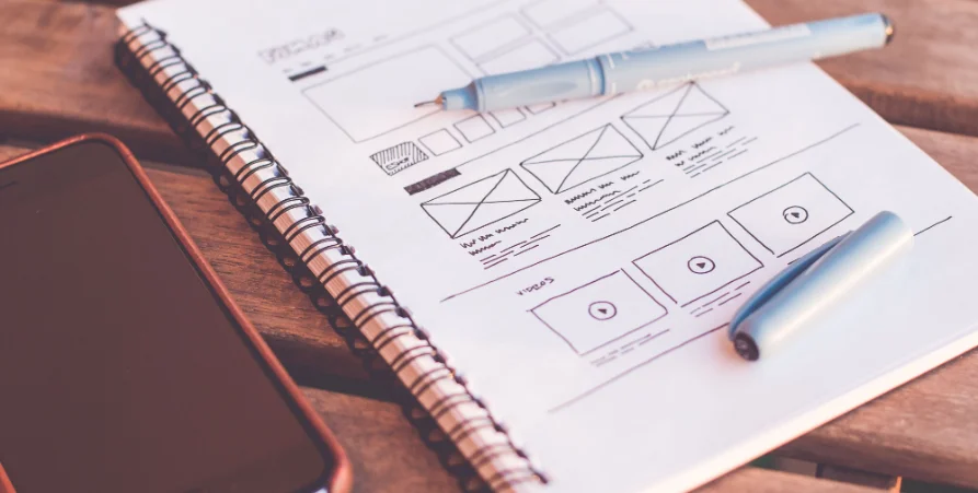 Croquis de maquette d'application sur un carnet à spirale, à côté d'un smartphone